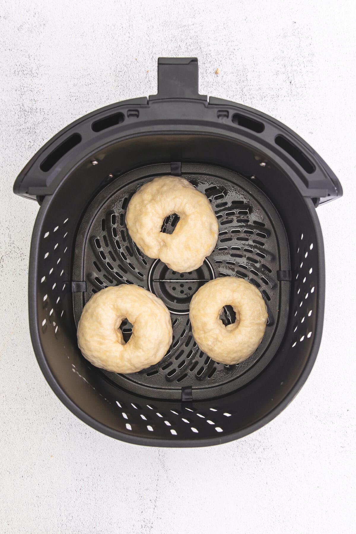 3 uncooked bagels in air fryer basket