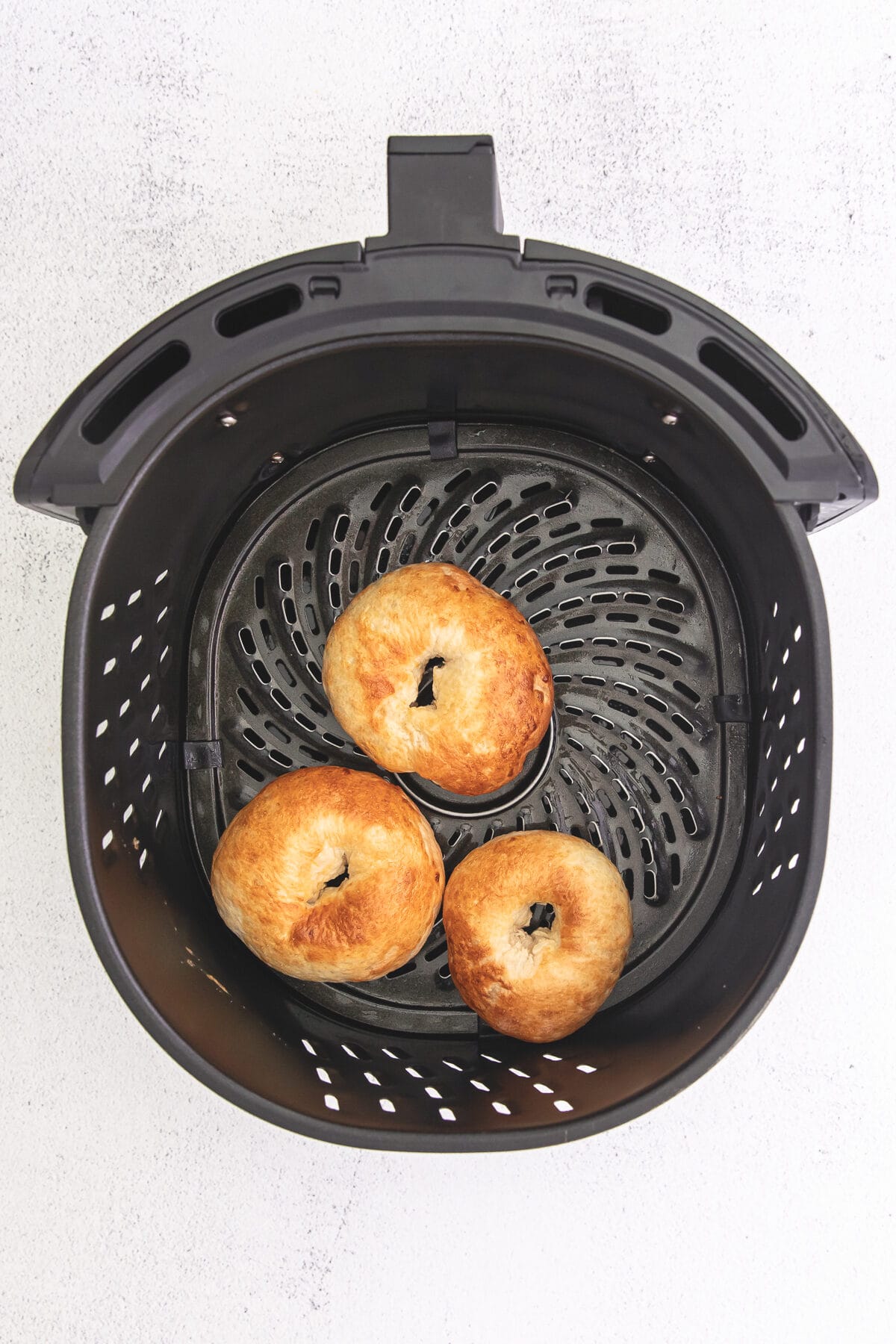 3 cooked bagels in air fryer basket.