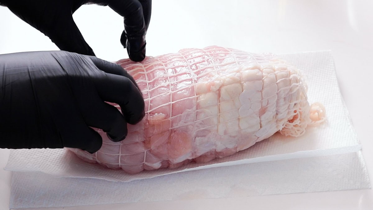 hands loosening netting and moving skin down to cover the boneless turkey breast.