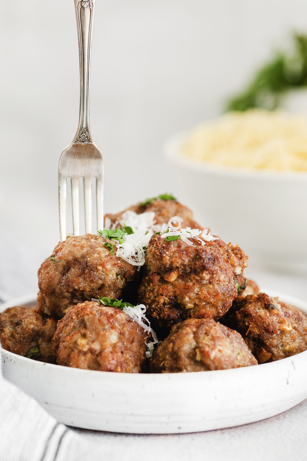 fork sticking into a meatball on a white low bowl full of air fryer meatballs.