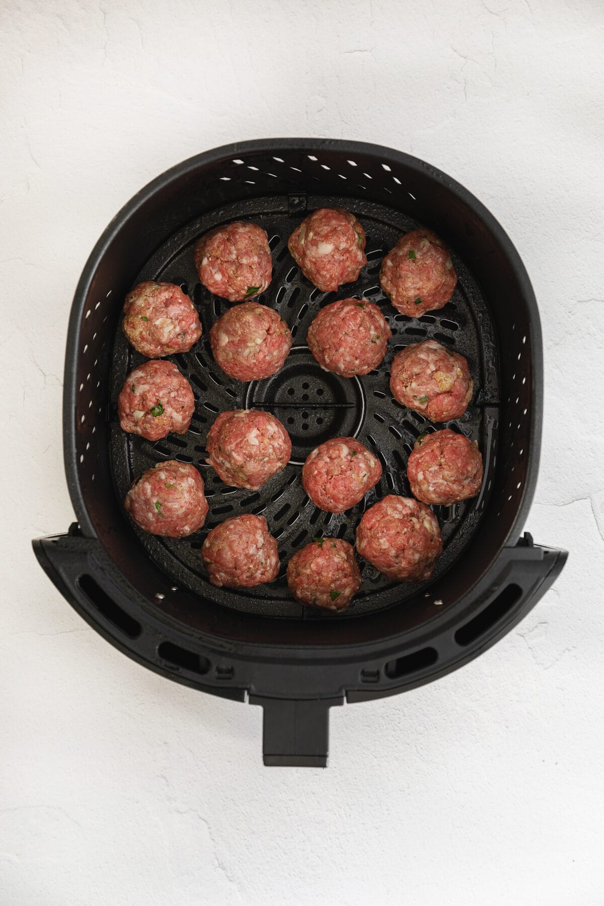 raw meatballs in air fryer basket.