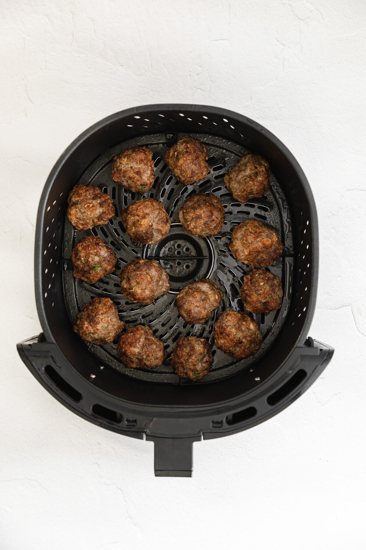 cooked meatballs in air fryer basket.