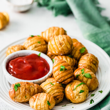 air fryer mini hasselback potatoes on a white plate with a small bowl of ketchup to the left.