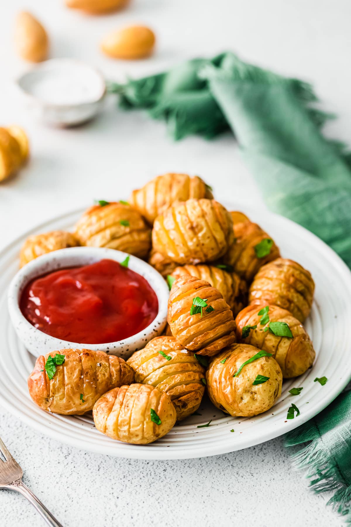 air fryer mini hasselback potatoes on a white plate with a small bowl of ketchup to the left.