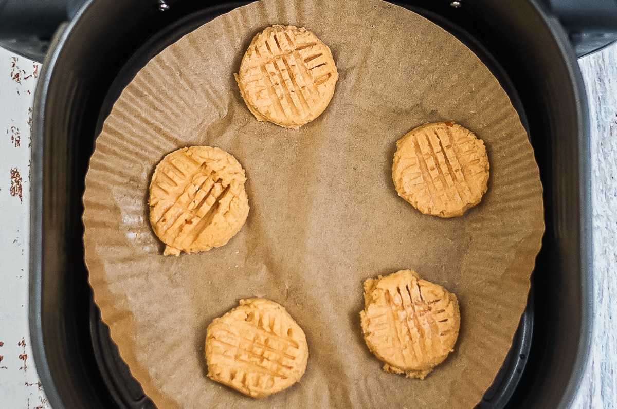 unbaked cookies in air fryer basket on parchment paper.