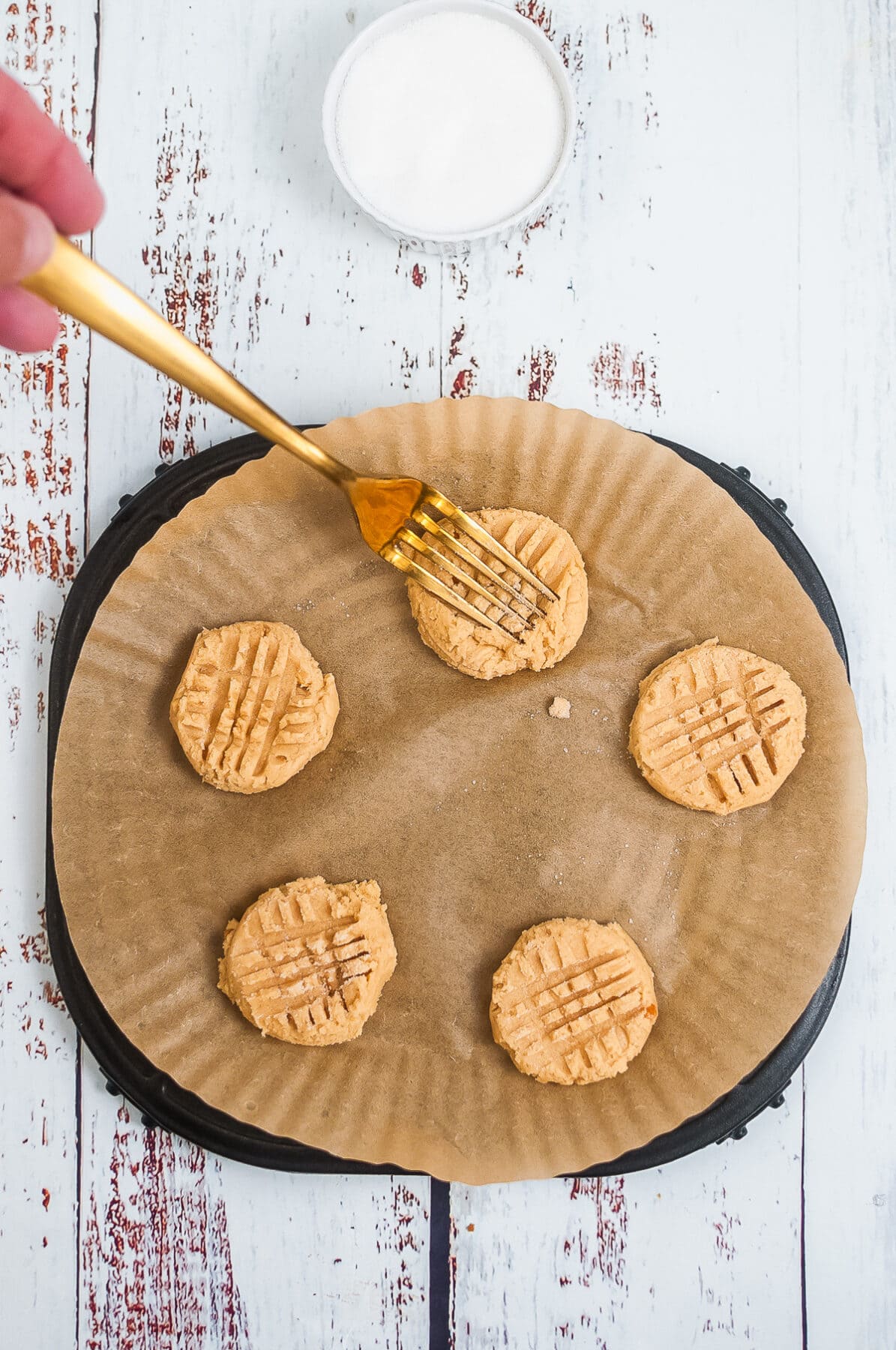 fork making lines in peanut butter cookies on a parchment lined plate.