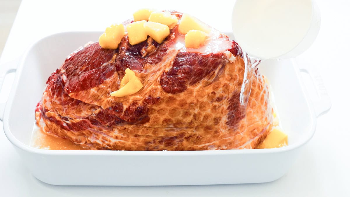 pouring water around ham in casserole dish.