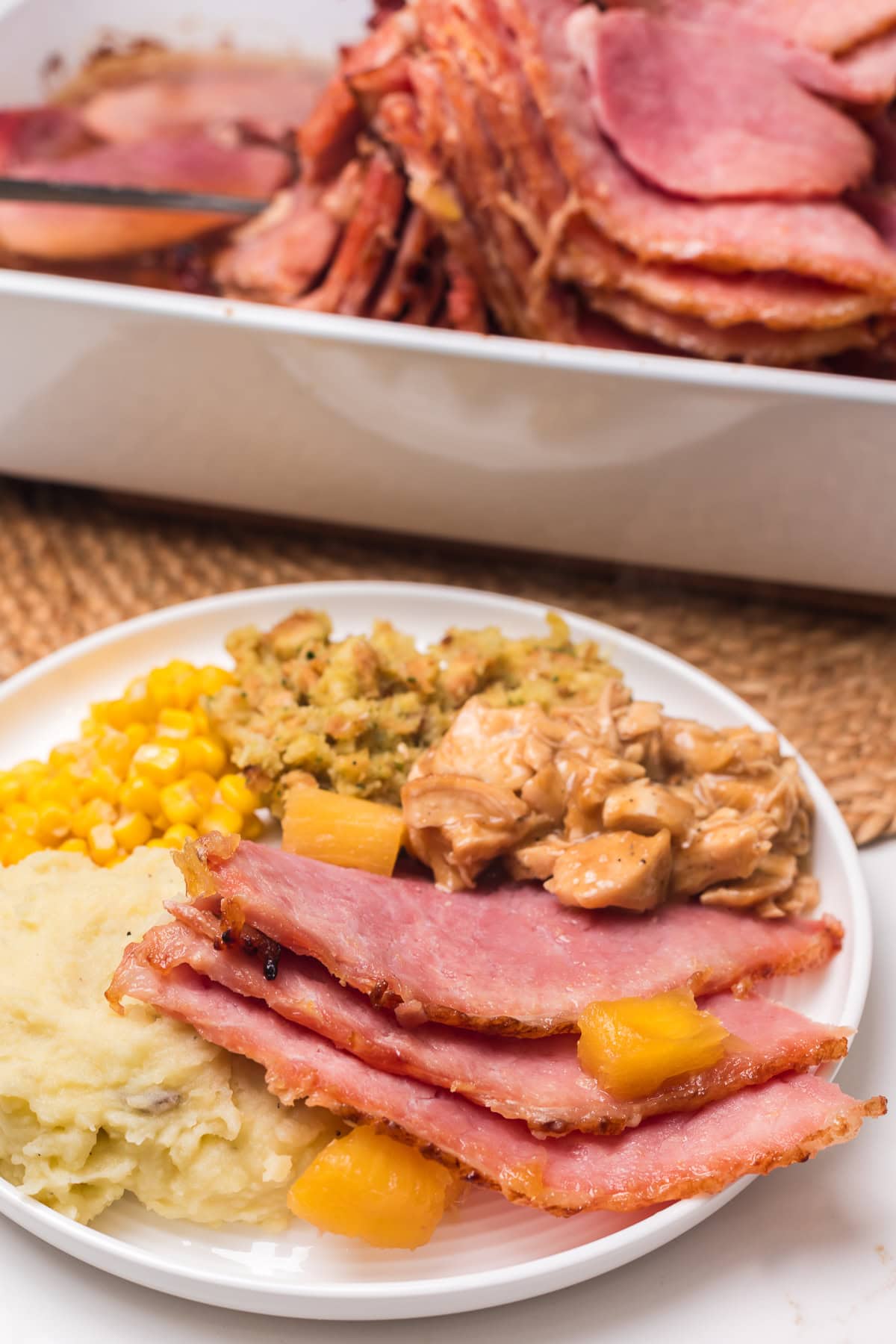 plate of thanksgiving dinner with baked ham, turkey and gravy, buttered corn, mashed potatoes and stuffing.