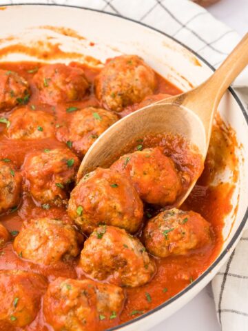 Baked Italian meatballs in a pan with spoon scooping two meatballs.