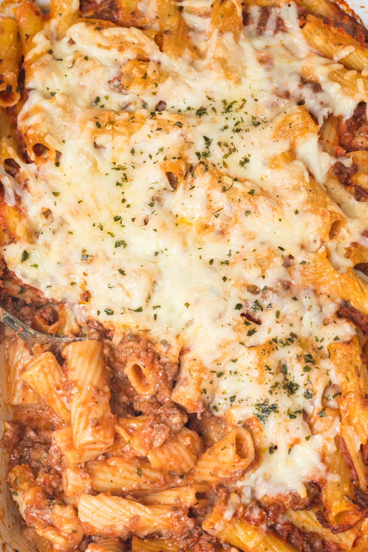 homemade baked ziti without ricotta in a white casserole dish with a scoop taken out and serving spoon in its place.