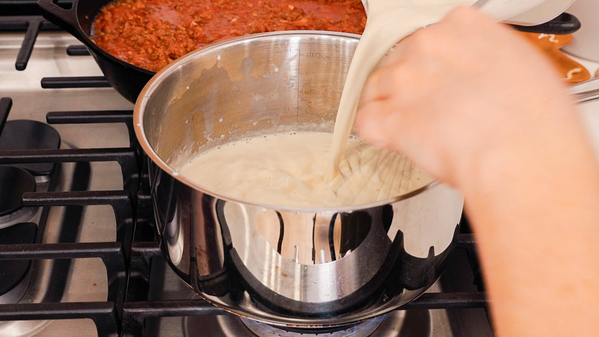 whisking milk into saucepan to make a bechamel sauce.