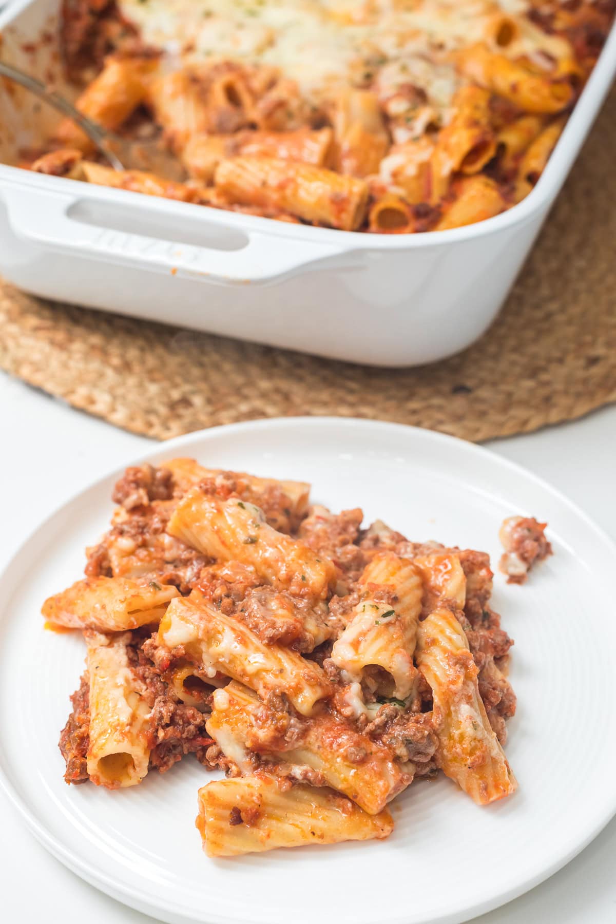 baked ziti on a plate with the casserole dish behind it.