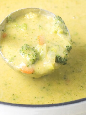 broccoli cheddar soup in a ladle over a dutch oven full of soup.