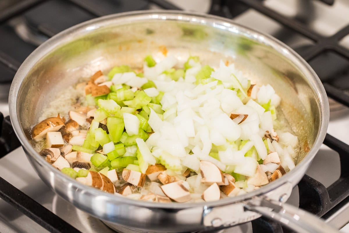 celery, onions, and mushrooms in melted butter in a skillet on the stove.