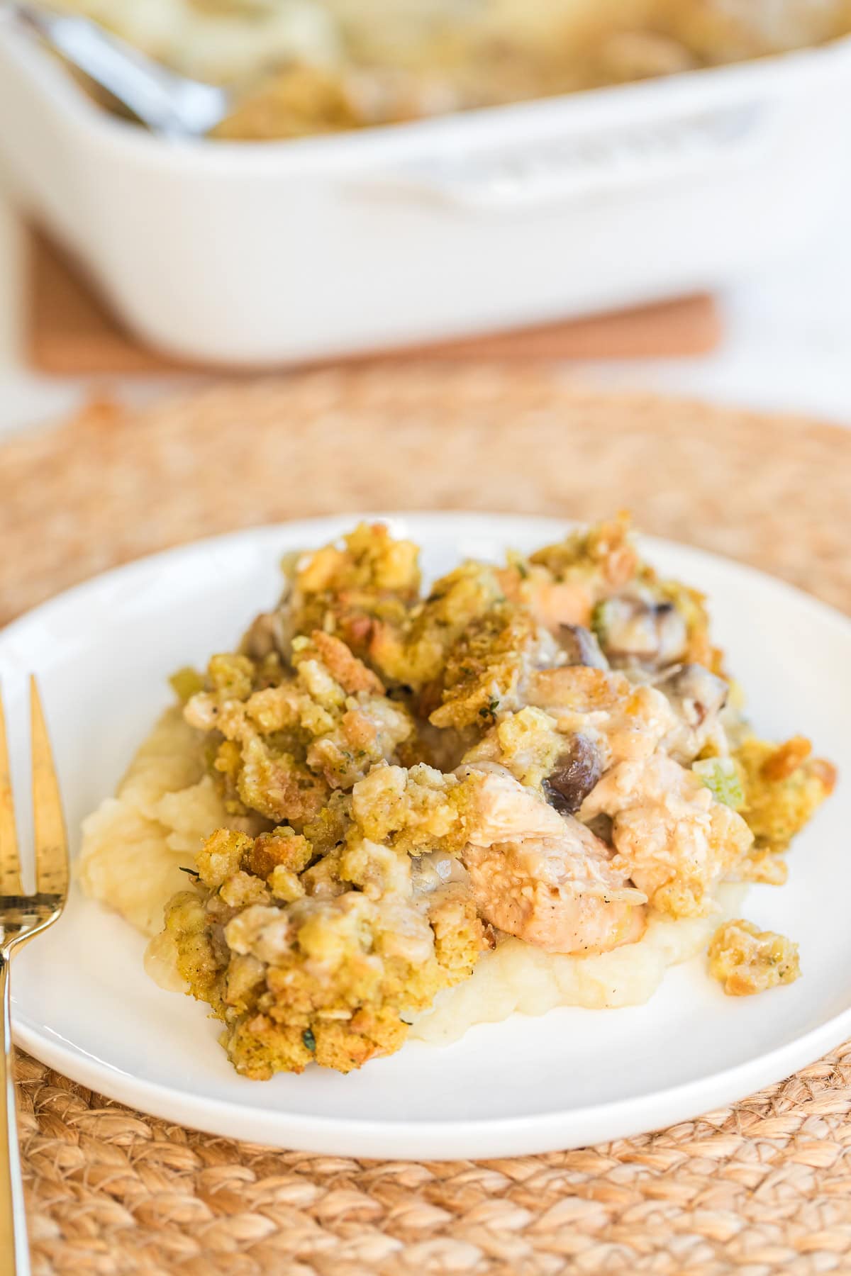 chicken and stuffing casserole served over mashed potatoes on a white plate with a gold fork.