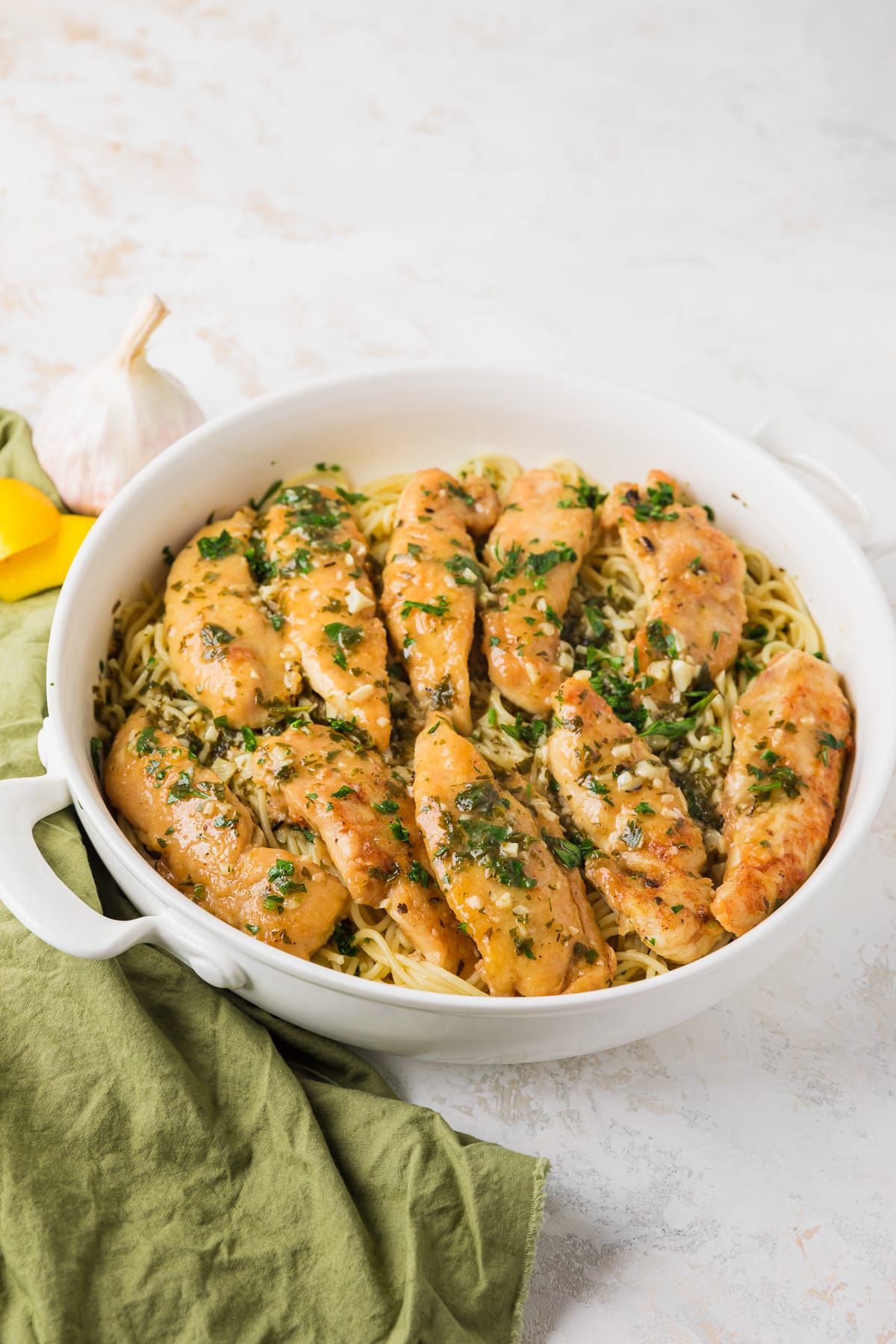 chicken scampi pasta in a white serving dish with a green napkin next to it.