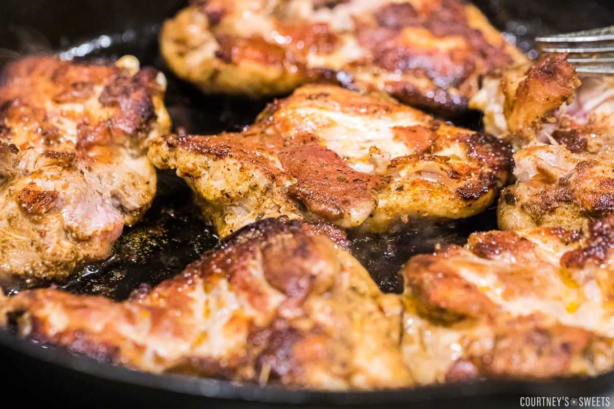 chicken thighs cooking in cast iron pan