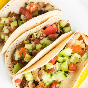 chicken tacos on a white plate with cucumber and tomato salsa