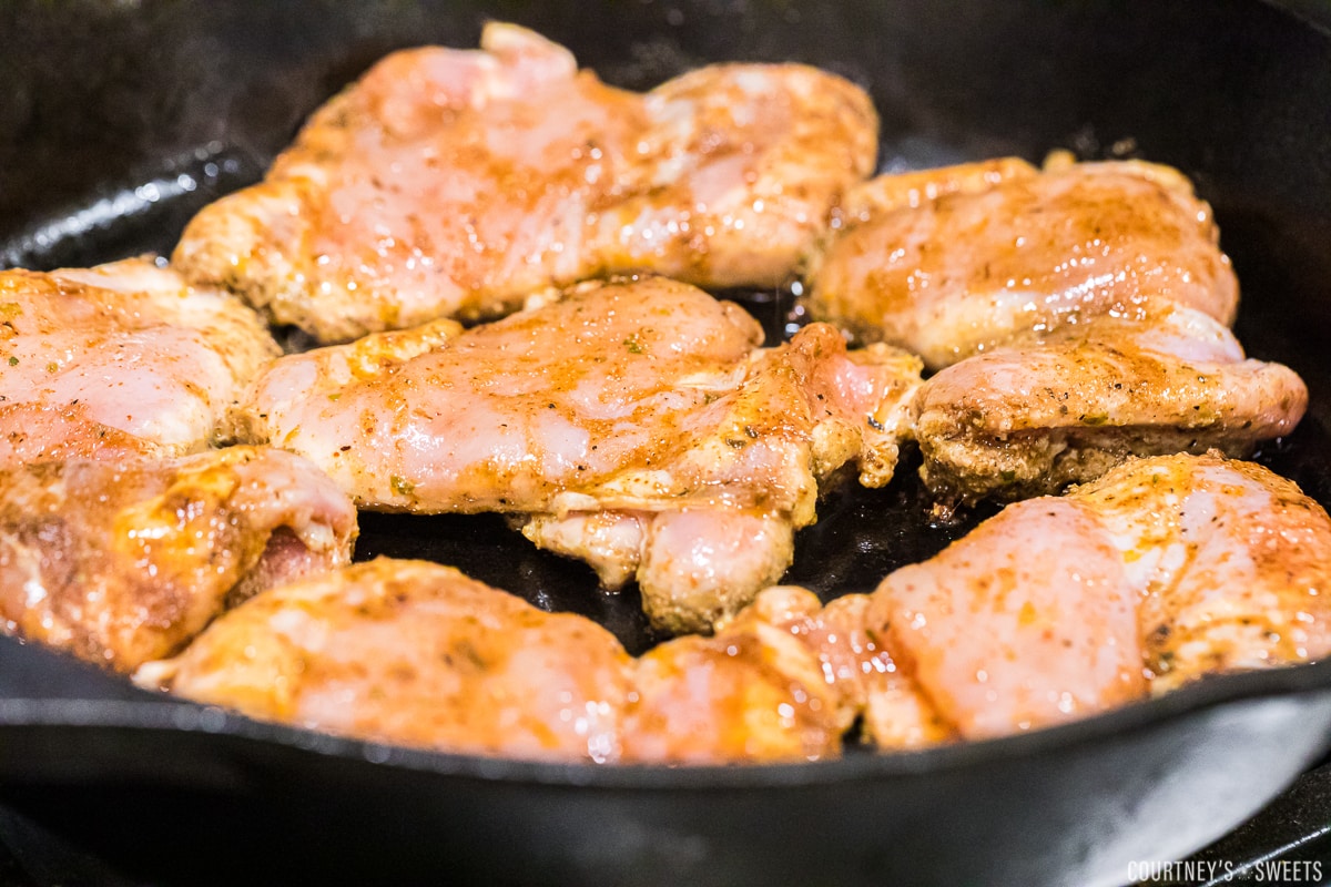 seasoned skinless boneless chicken thighs in cast iron pan cooking