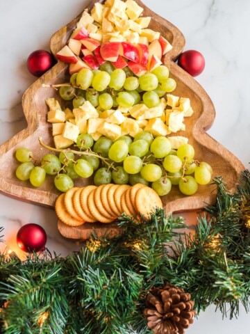 christmas tree cheese platter with fruit, cheese, and crackers chopped on a christmas tree shaped board with garland on the bottom for decoration