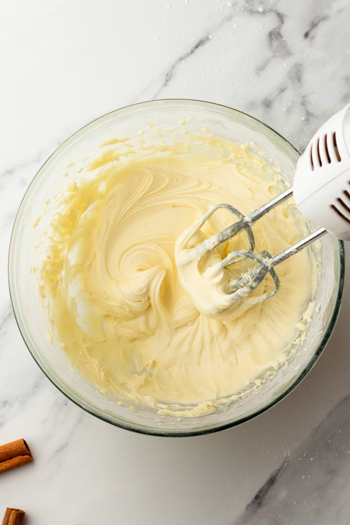 cinnamon roll cream cheese frosting in a glass bowl with electric beaters.