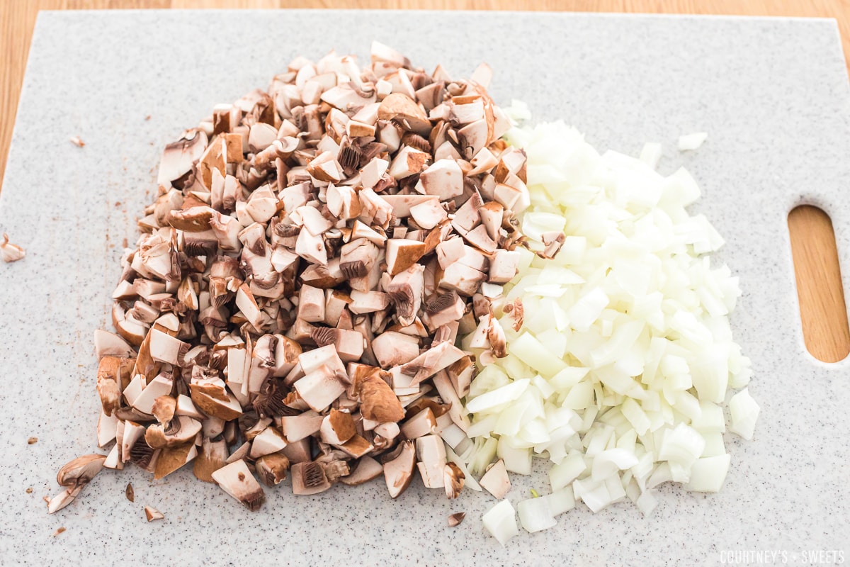 chopped mushrooms and onions on a cutting board.