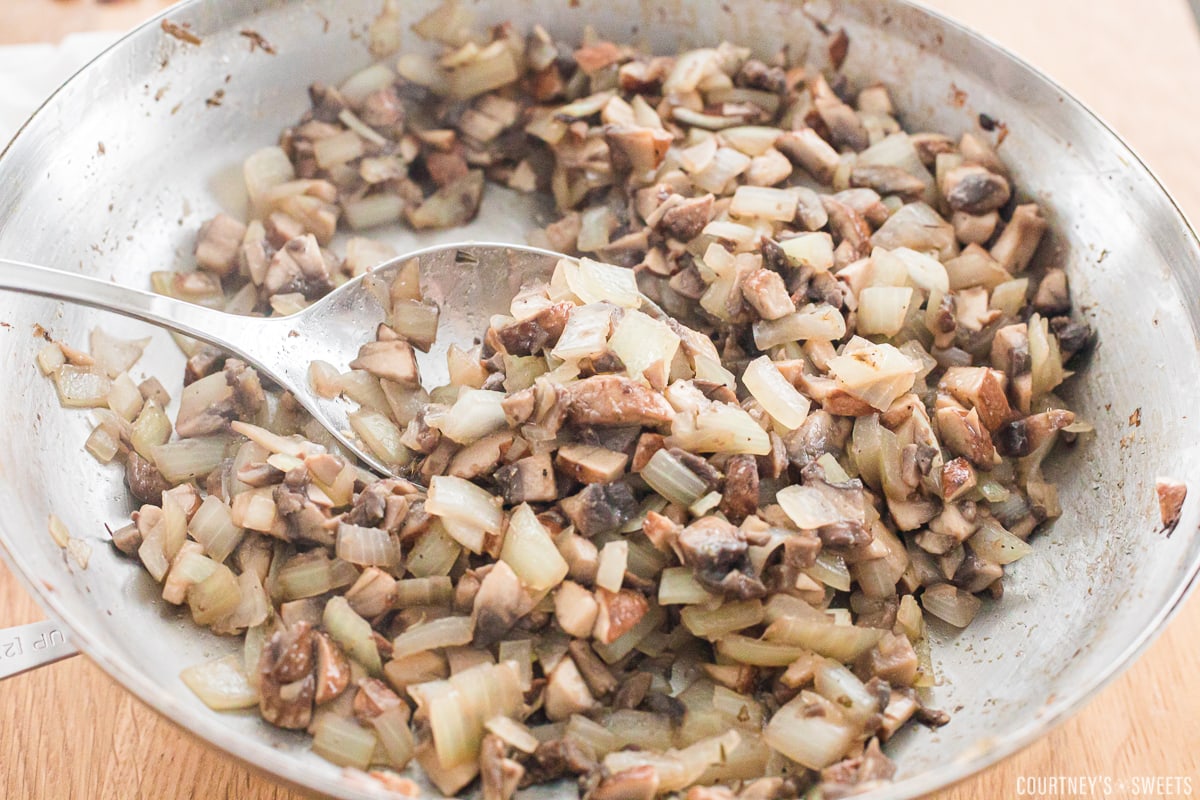 cooked mushrooms and onions in a skillet with a spoon.