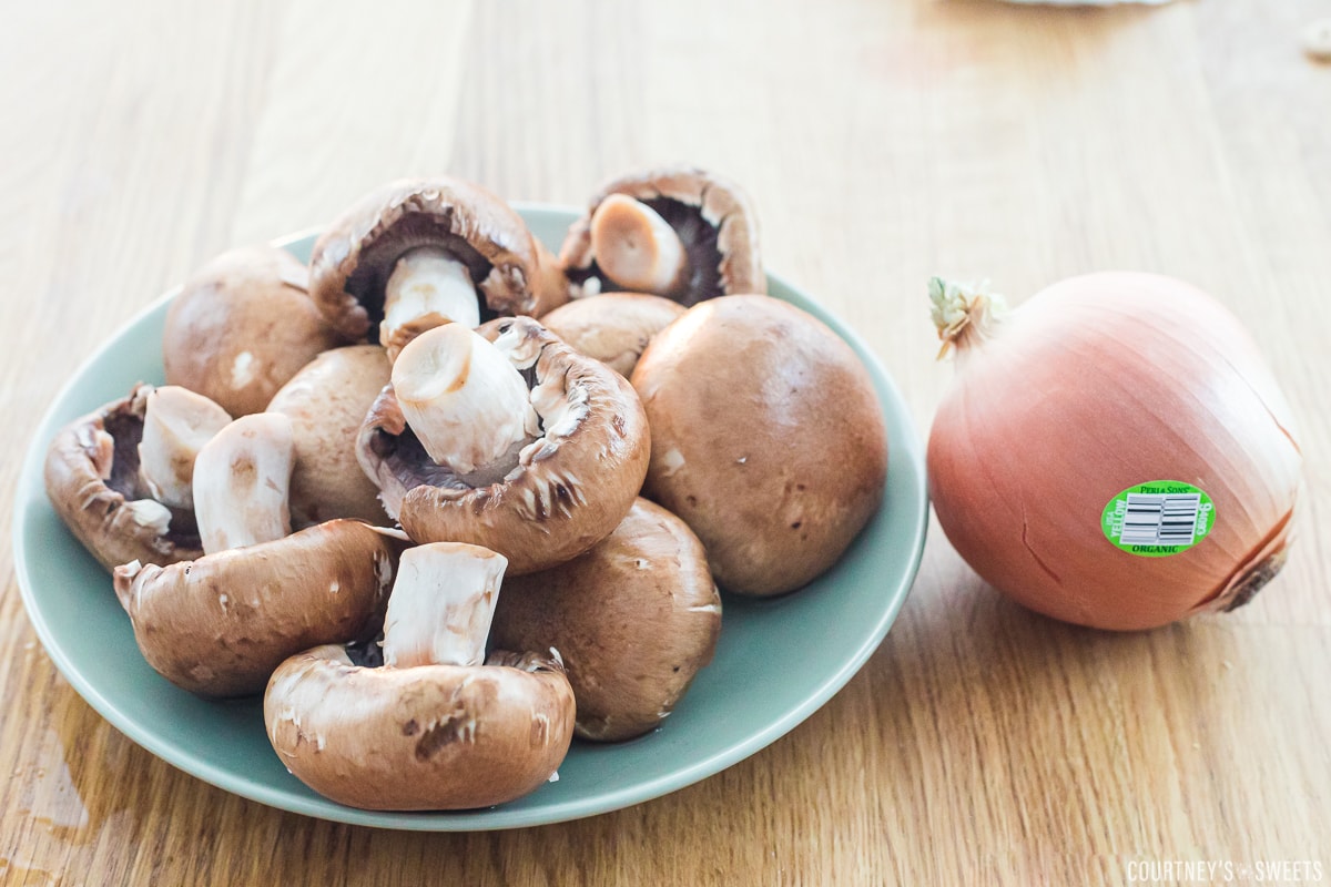 baby bell mushrooms on a plate next to an onion on the counter.