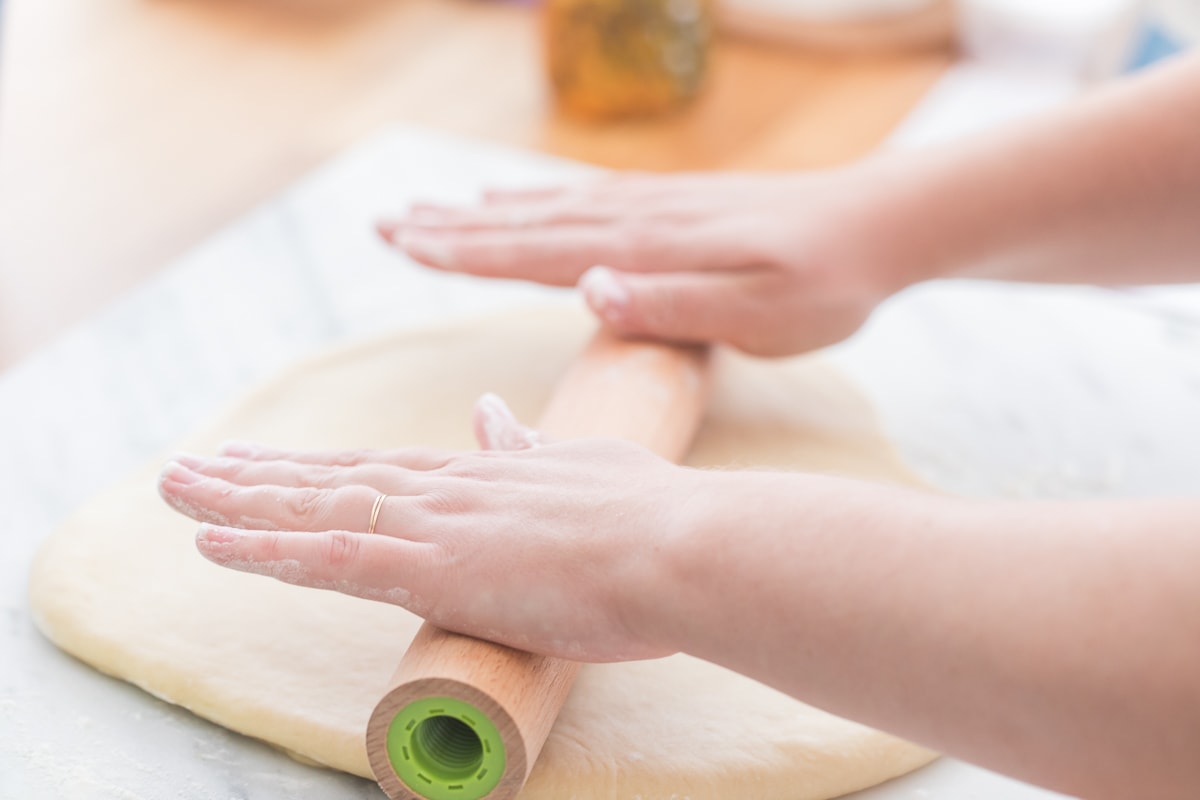 hands rolling out donut dough.