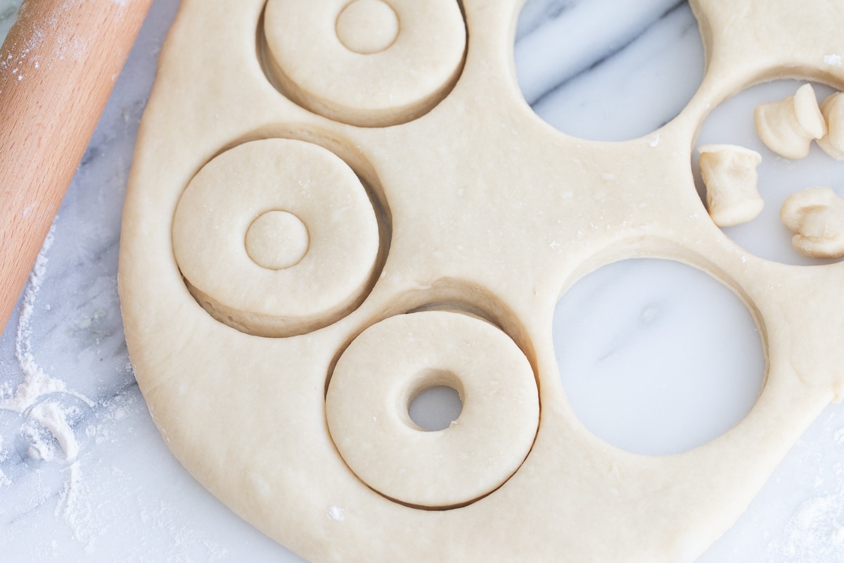 donut cut outs in dough on a marble pastry board.