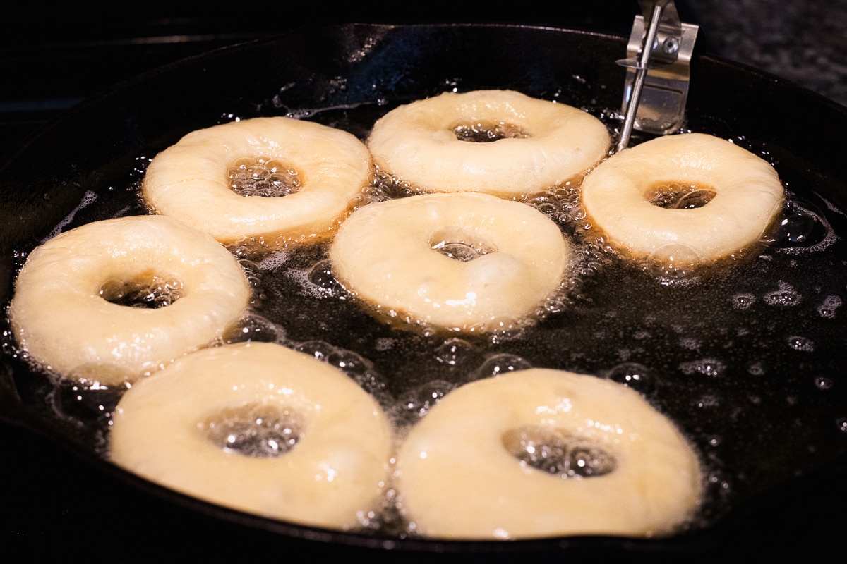 donuts frying in a cast iron pan with oil.