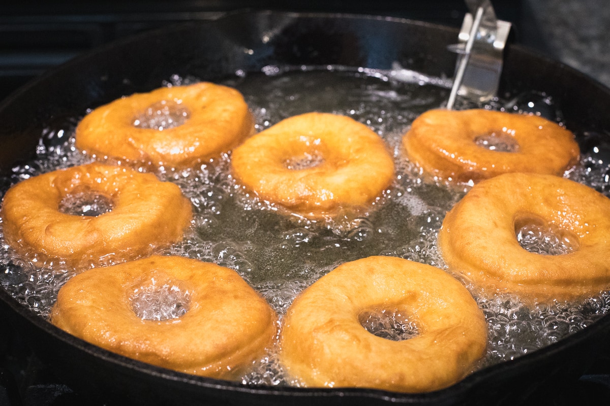 golden brown donuts frying in oil in a cast iron skillet.