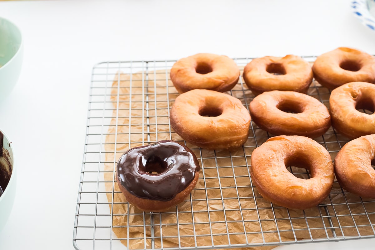 donuts on a cooling rack and one donut covered with chocolate frosting.