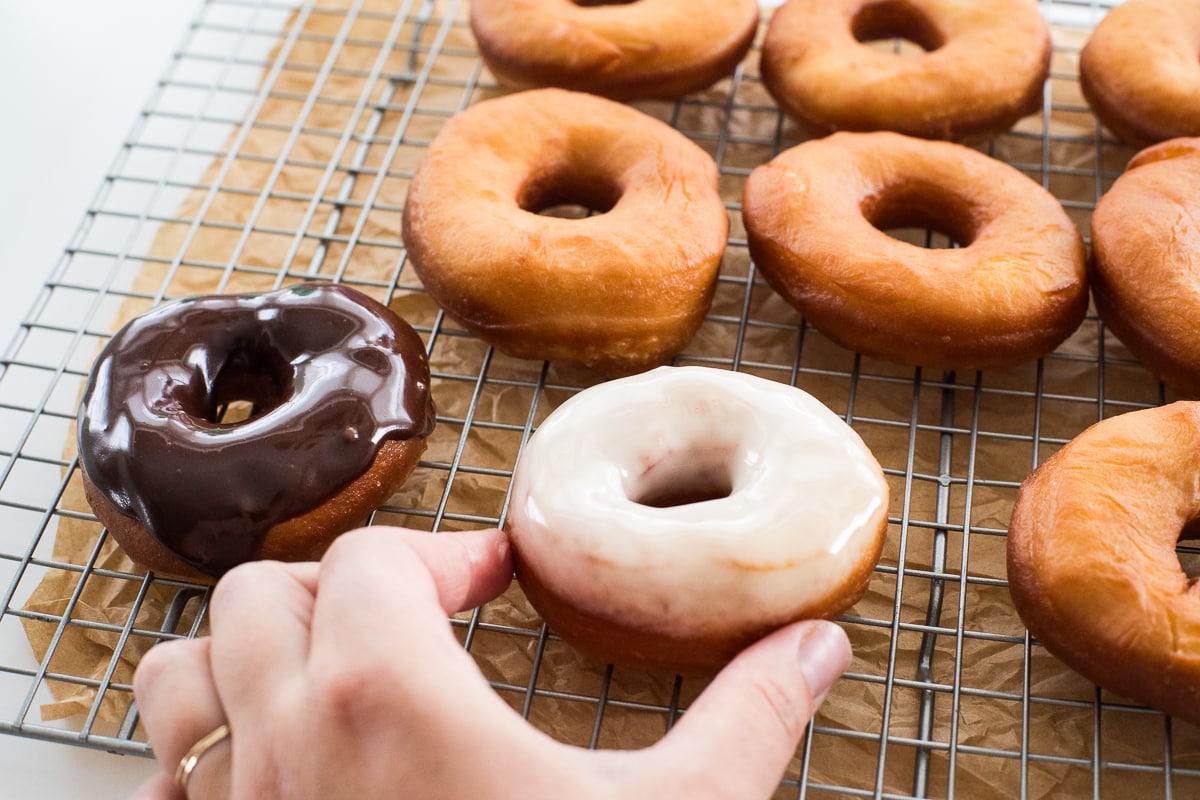 hand placing glazed donut onto a cooling rack with more donuts.