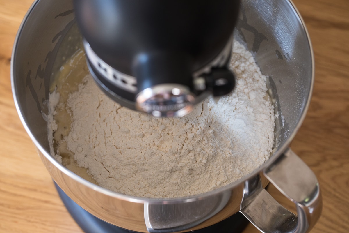 over head photo of ingredients in a black stand mixer in a stainless steel bowl to make donuts.