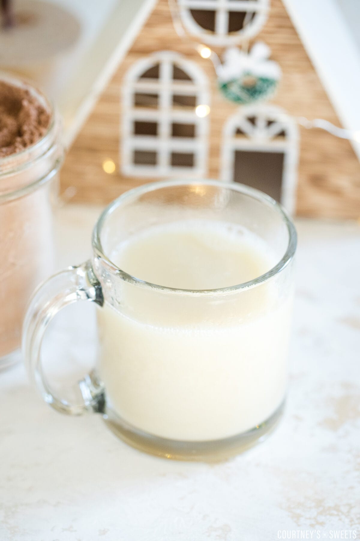 warm oat milk in a glass mug with little christmas house behind it