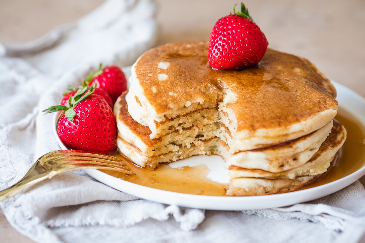 stack of pancakes covered in syrup with a strawberry on top.