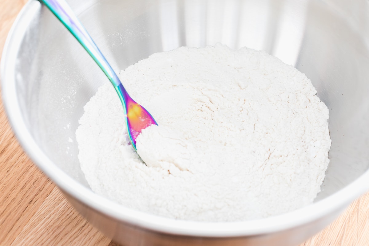 dry ingredients for pancakes in a stainless steel bowl with a rainbow utensil.