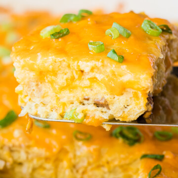 easy breakfast casserole topped with cheese and garnished with green onions on a serving spatula.