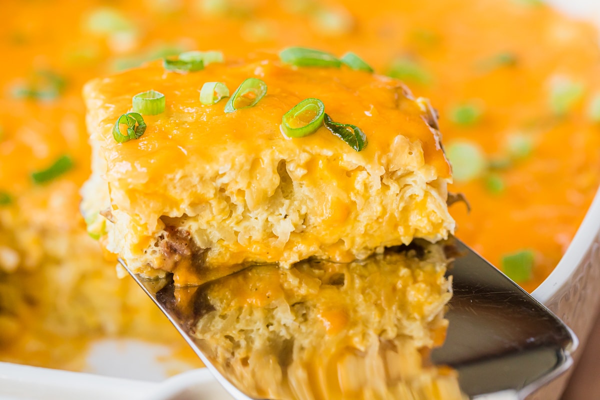 breakfast casserole topped with cheese and garnished with green onions on a serving spatula.