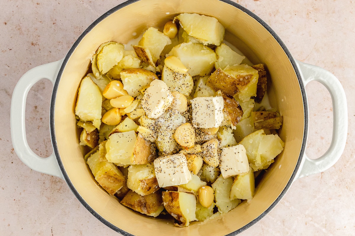 dutch oven with boiled potatoes, butter and garlic, ready to mash.