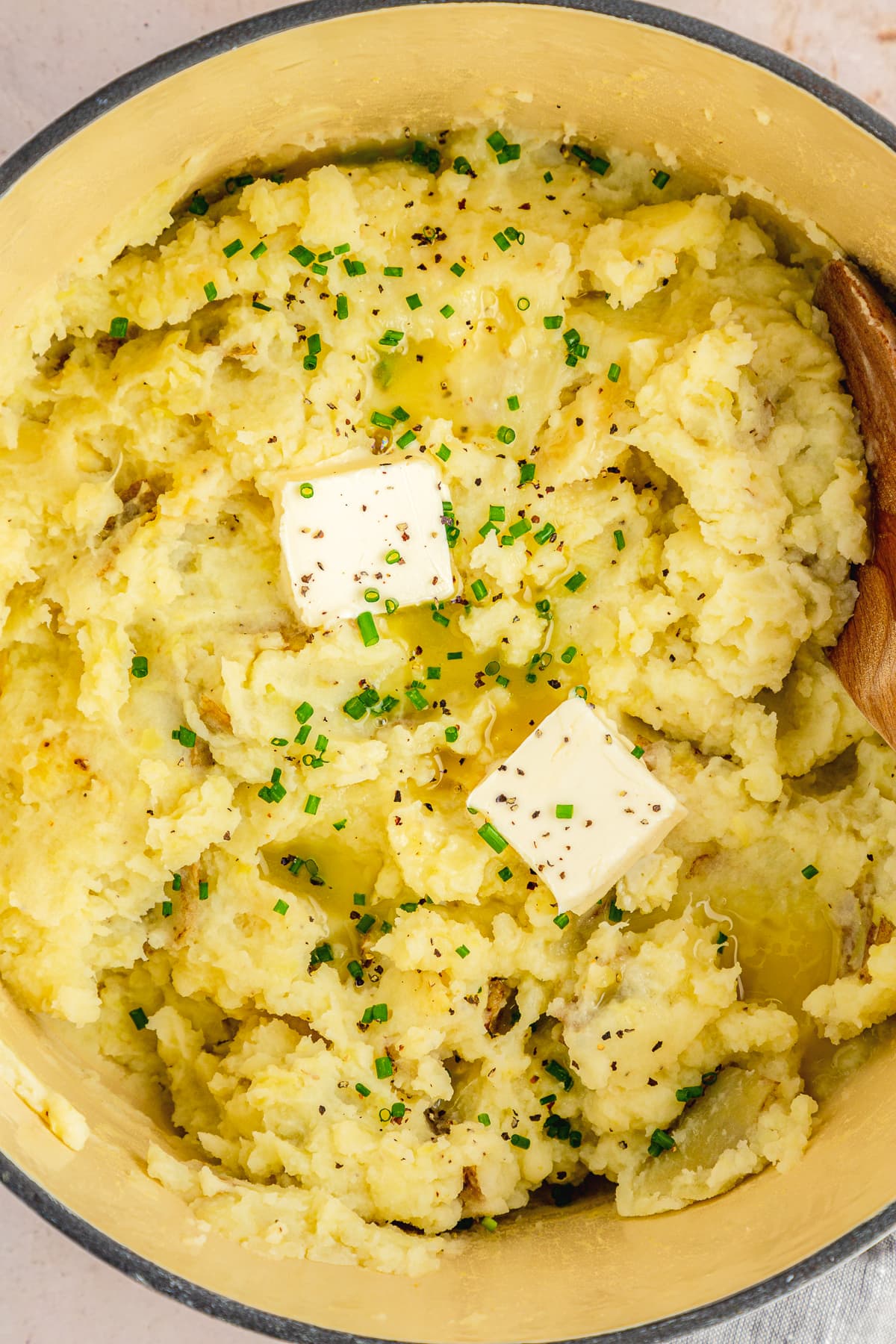 garlic mashed potatoes in a dutch oven with two pats of butter and chive chopped garnish.