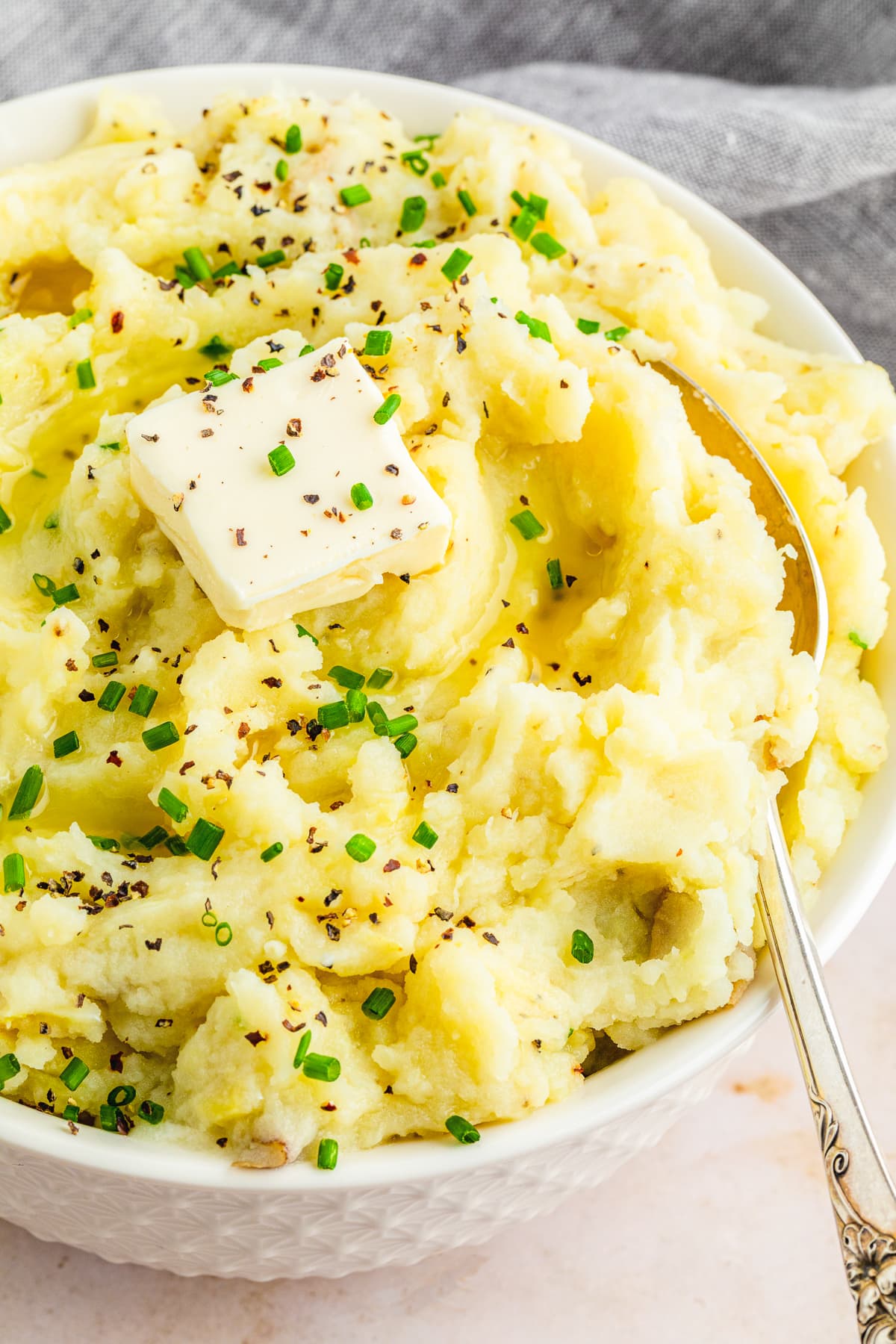 garlic mashed potatoes in a white bowl with a pat of dairy free butter and chives as garnish and a spoon to the right inside the bowl.