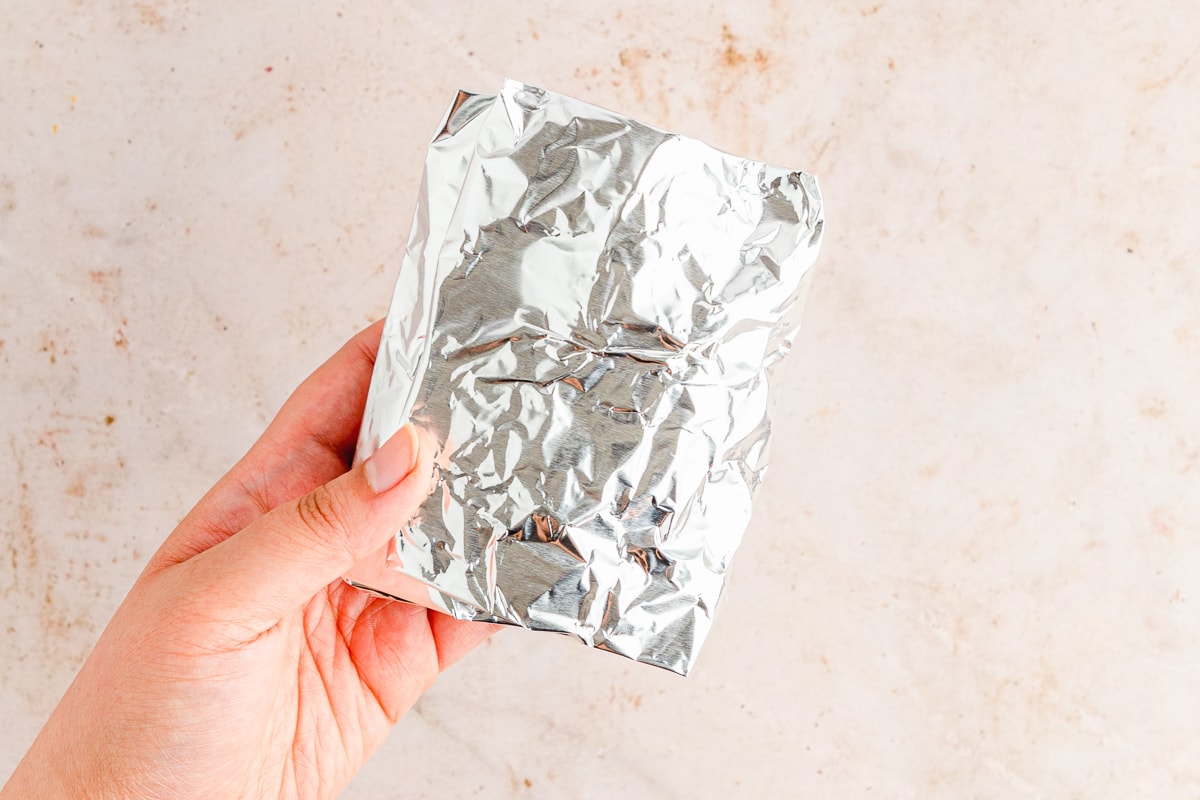 hand holding a garlic bulb wrapped in aluminum foil.