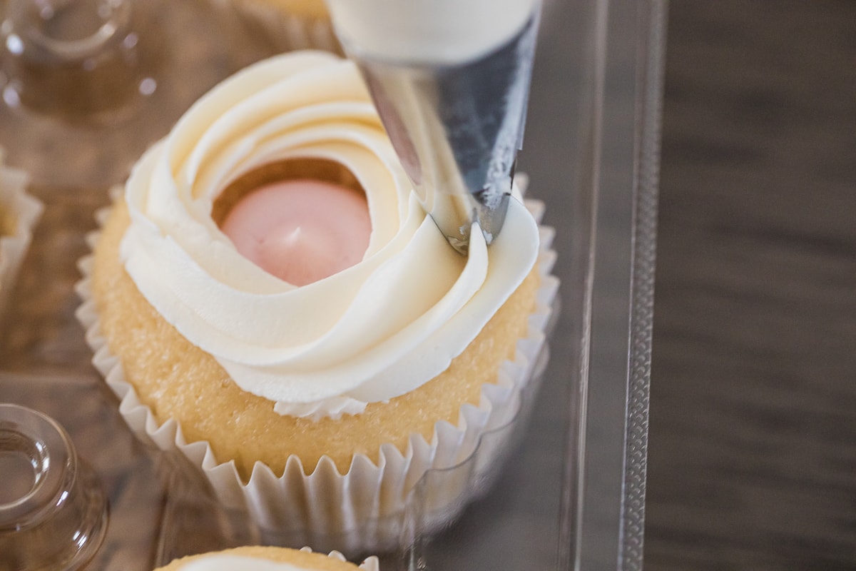 piping frosting over cupcakes filled with pink frosting in the center.