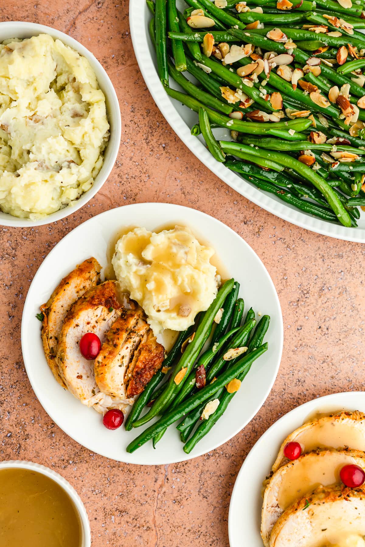 green beans almondine on a white plate with roasted turkey breast slices, cranberries, and mashed potatoes with gravy.