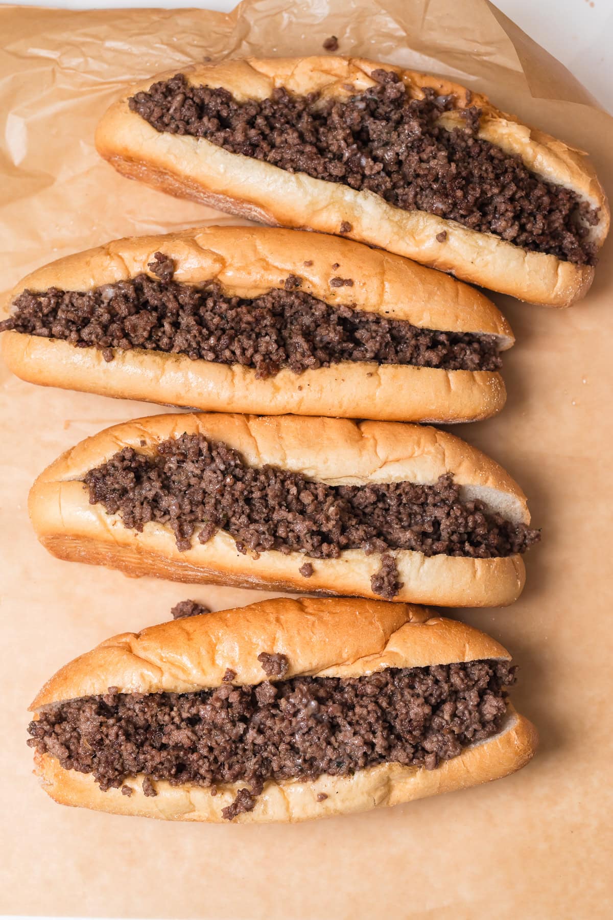 over head photo of 4 ground beef cheeseteak on parchment paper.