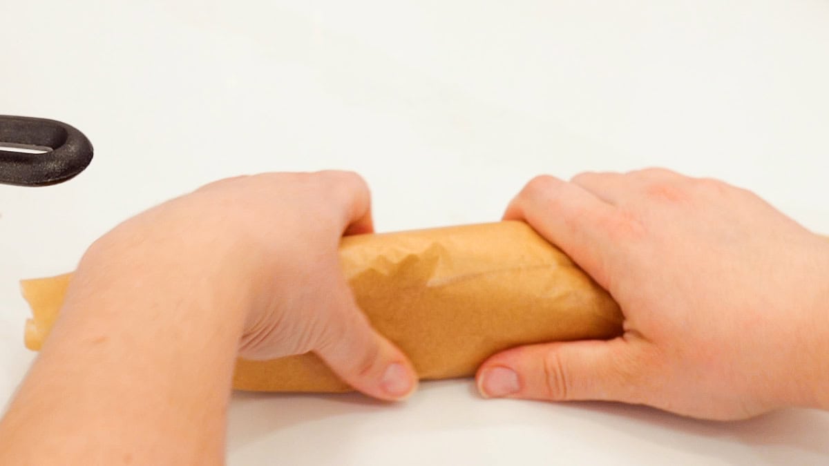 hands holding rolled up ground beef cheesesteak in parchment paper.