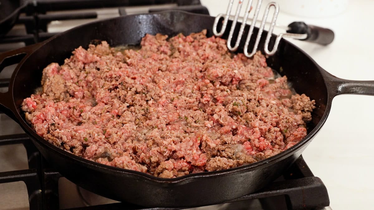 partially brown ground beef in a cast iron skillet.