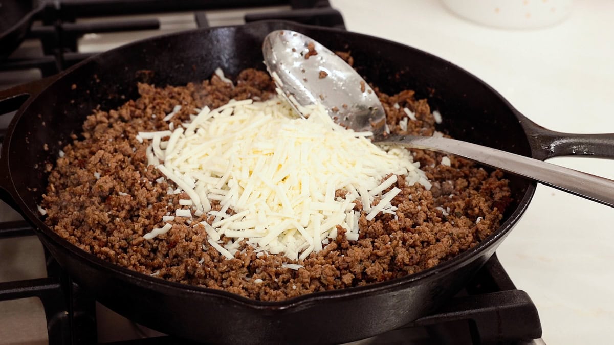 browned ground beef in a skillet with shredded mozzarella on top.